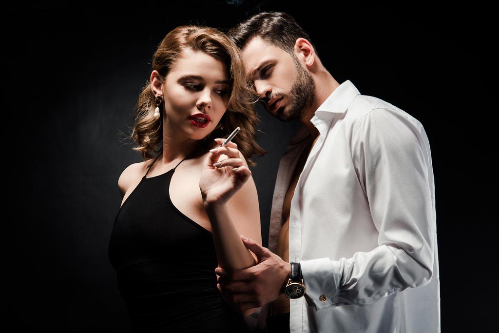 jóképű férfi fehér kigombolt ing megható szexi, elegáns nő kezében cigaretta fekete háttér - Fotó, kép
