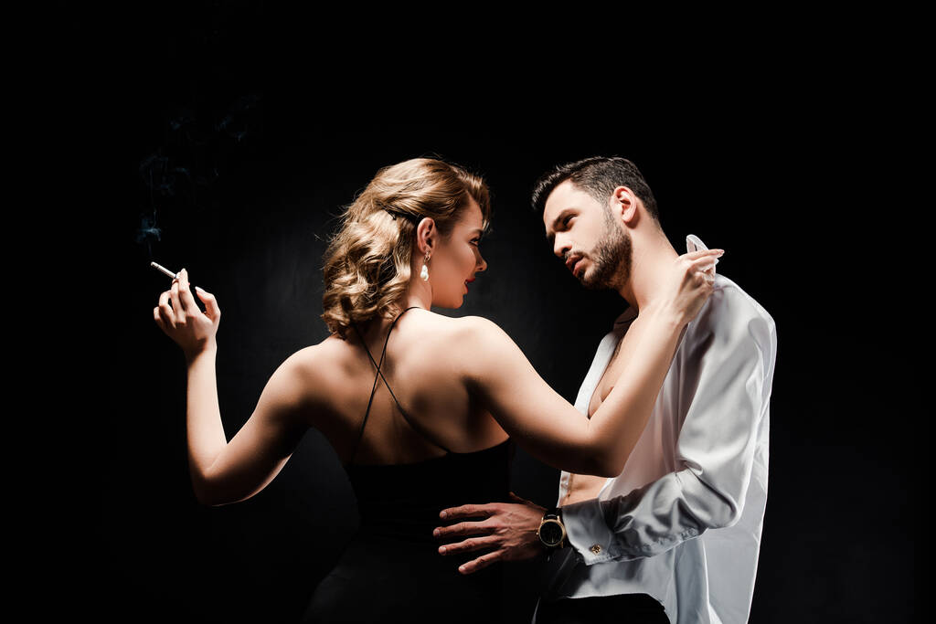 sexy, elegante donna in possesso di sigaretta e spogliarsi bell'uomo isolato su nero
 - Foto, immagini