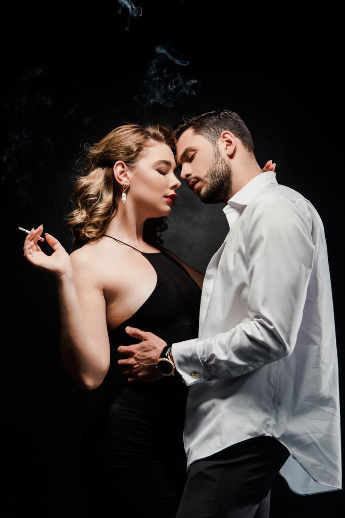 白いシャツのハンサムな男は魅力的でエレガントな女性を受け入れます黒で隔離されたタバコを保持 - 写真・画像