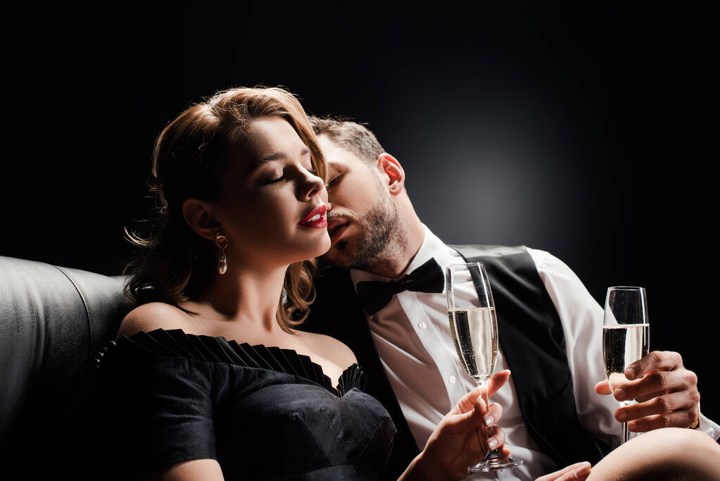 élégant homme baisers séduisante, belle femme assise avec les yeux fermés sur fond noir
 - Photo, image