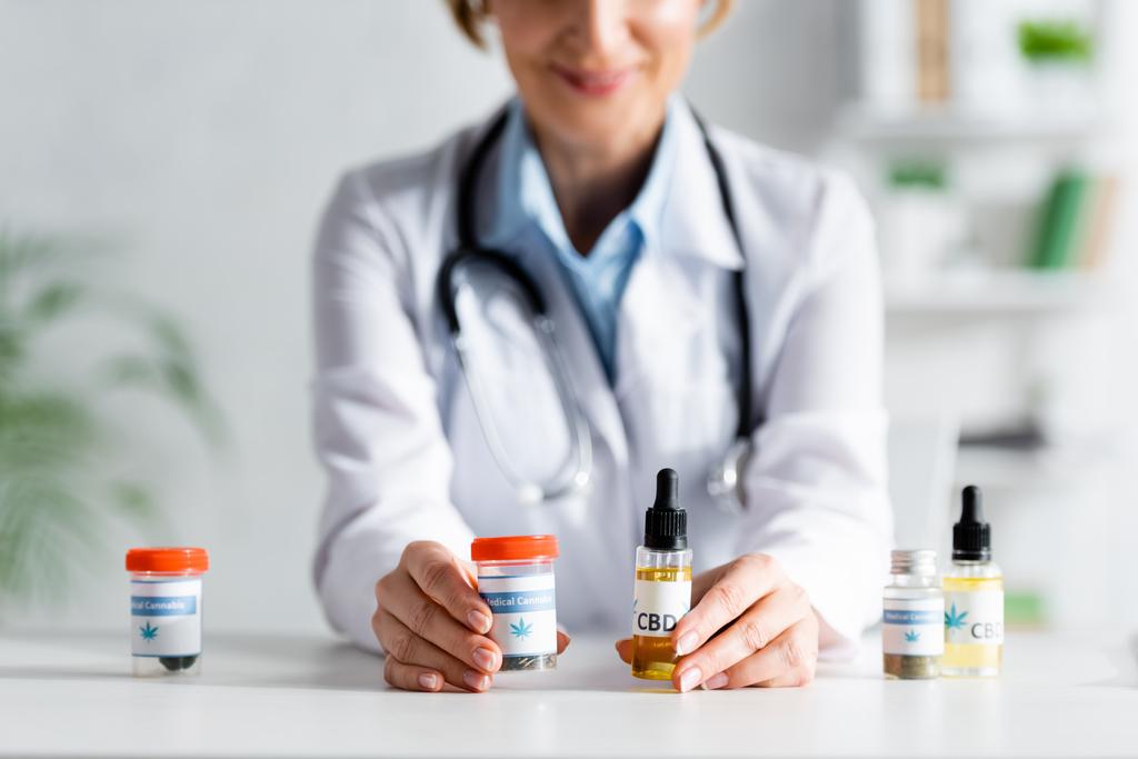 vue recadrée du médecin en manteau blanc tenant des bouteilles avec cbd et lettrage de cannabis médical
  - Photo, image