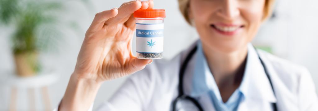 panoramiczne ujęcie wesołego i dojrzałego lekarza w białym płaszczu trzymającego butelkę z medycznym napisem marihuany  - Zdjęcie, obraz