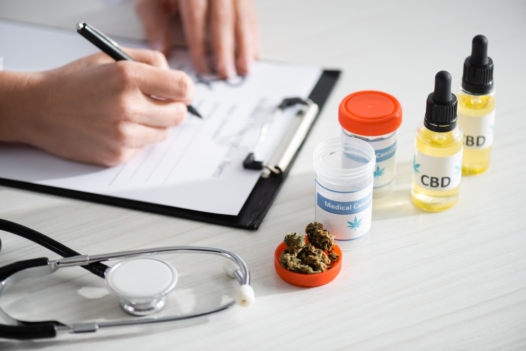 bijgesneden weergave van arts schrijven recept in de buurt van gedroogde wiet, flessen met cbd en medische cannabis belettering  - Foto, afbeelding