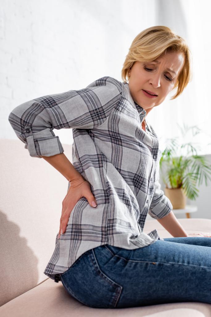 Reife Frau leidet unter Rückenschmerzen und sitzt auf Sofa  - Foto, Bild