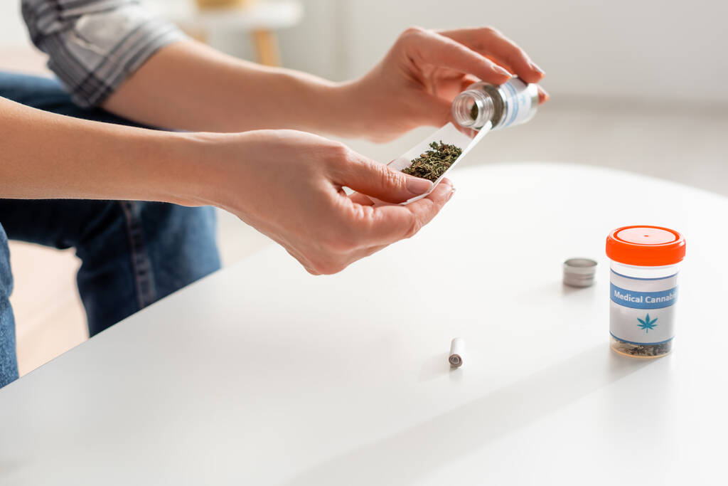 vista cortada de mulher madura segurando papel perto de garrafa com cannabis medicinal seca
  - Foto, Imagem