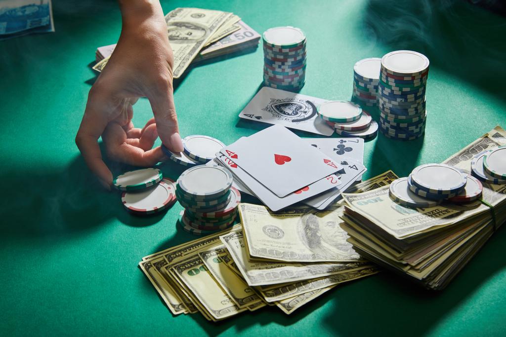Részleges kilátás a női kéz kaszinó zsetonok, játékkártyák és pénz zöld alapon - Fotó, kép
