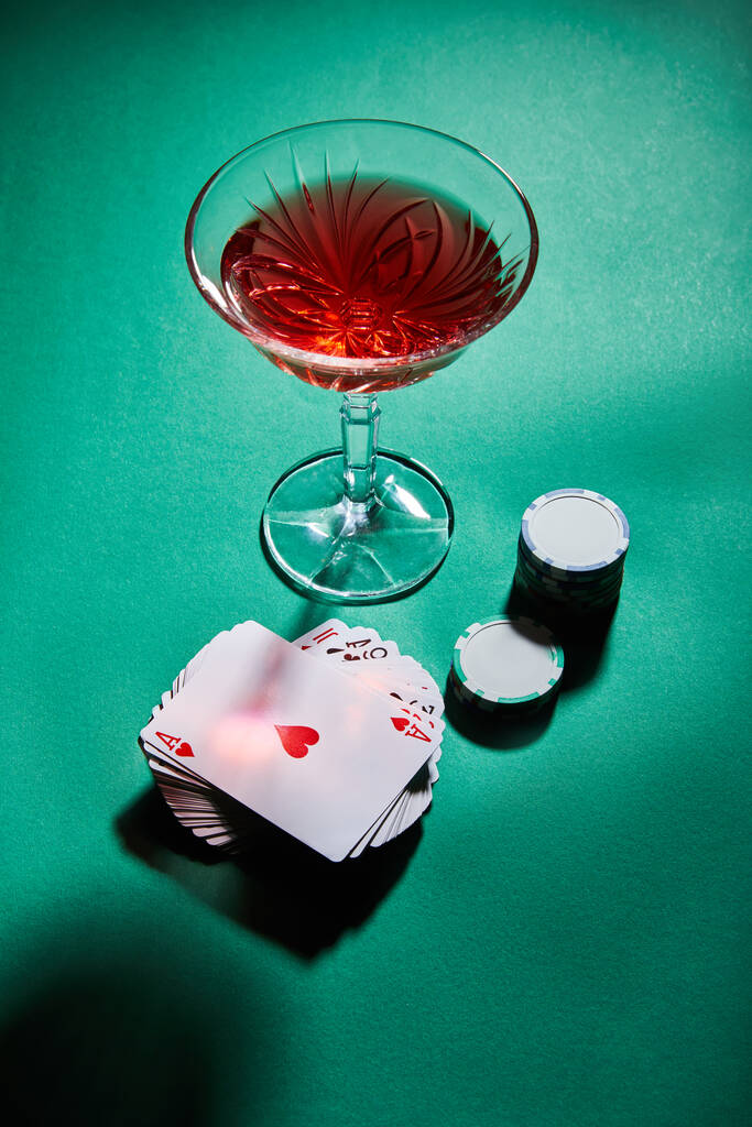 Vista di angolo alto di vetro di cocktail vicino a carte da gioco e gettoni di casino su verde
 - Foto, immagini