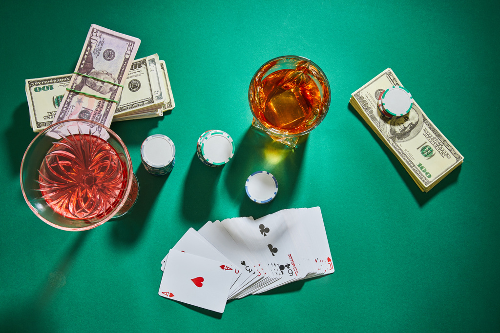 Draufsicht auf Cognac- und Cocktailgläser mit Geld, Spielkarten und Casino-Chips auf Grün - Foto, Bild