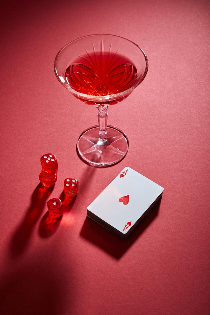 Vista di angolo alto di vetro di cocktail vicino a mazzo di carte e dadi su sfondo rosso
  - Foto, immagini