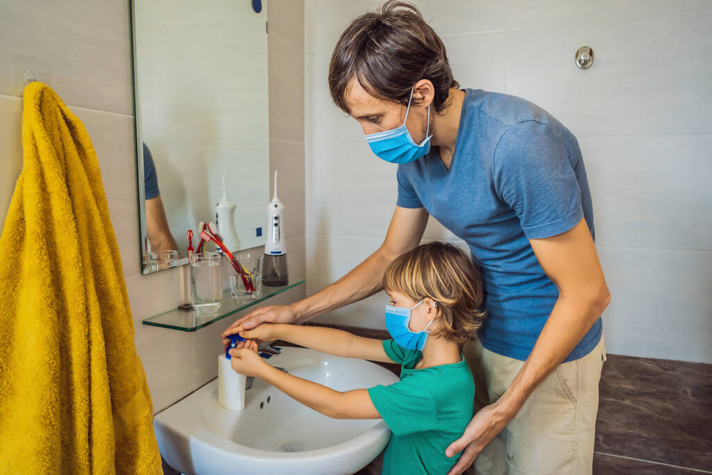 Papa bringt seinem Sohn bei, sich die Hände richtig zu waschen. Vater und Sohn in medizinischen Masken wegen Coronovirus. Epidemisch. Bleiben Sie zu Hause. Waschen Sie Ihre Hände - Foto, Bild