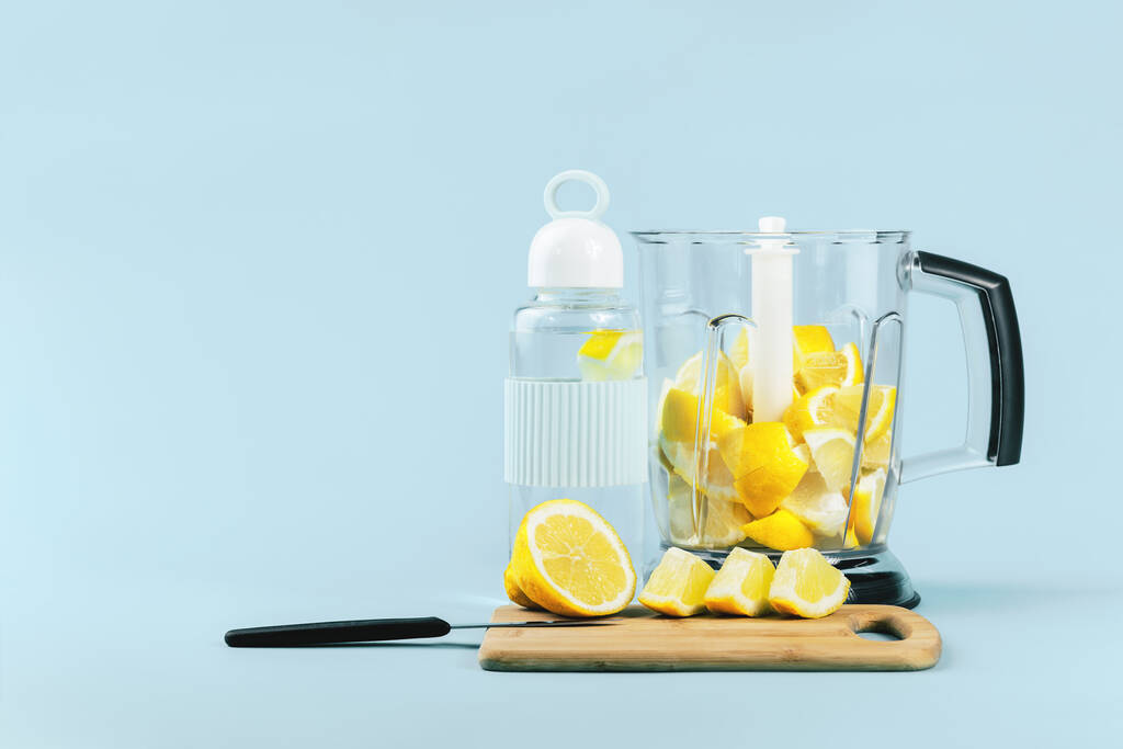 botella de cristal de agua de limón y una licuadora llena de pedazos de limones cortados de color amarillo brillante. Espacio de copia vista frontal. Estilo de vida saludable, control de peso y vitamina C inmune aumentan la hidratación o el concepto de batido
 - Foto, Imagen