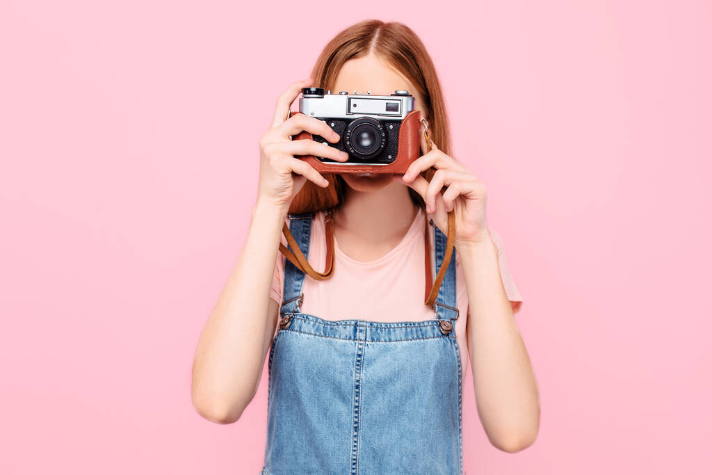 Aantrekkelijk stijlvol jong meisje maakt foto 's met een retro camera geïsoleerd op een roze achtergrond - Foto, afbeelding