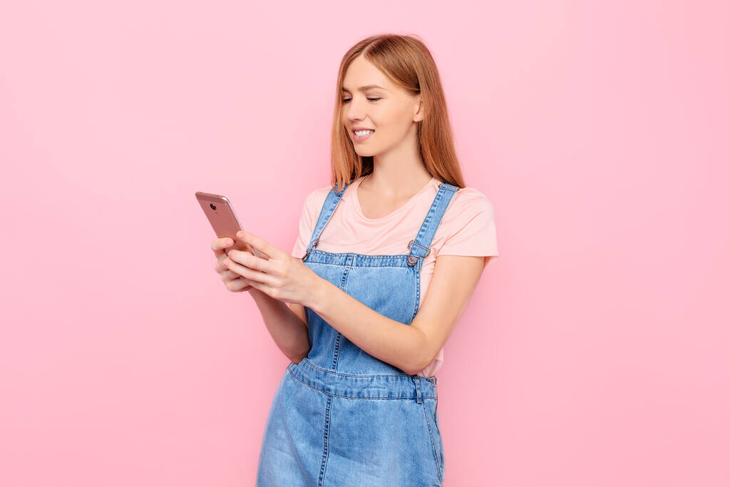 Attraktive junge stilvolle Frau schreibt eine Nachricht auf einem Smartphone auf einem isolierten rosa Hintergrund - Foto, Bild
