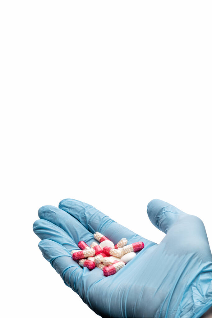 Χέρι σε ένα ιατρικό γάντι κρατώντας χάπια σε λευκό φόντο. Φάρμακο γρίπης. Θεραπεία μόλυνσης. Κοντινό πλάνο. Μεμονωμένα - Φωτογραφία, εικόνα