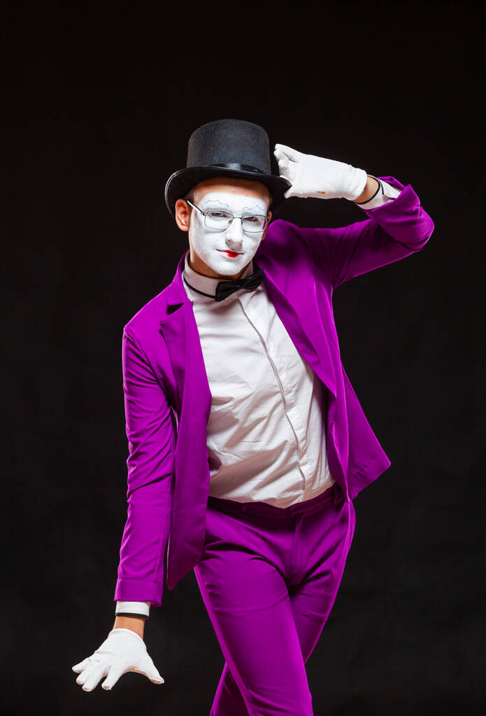 Портрет мужчины-пантомимы, изолированный на черном фоне. Человек в фиолетовом костюме с радостью позирует перед камерой
 - Фото, изображение