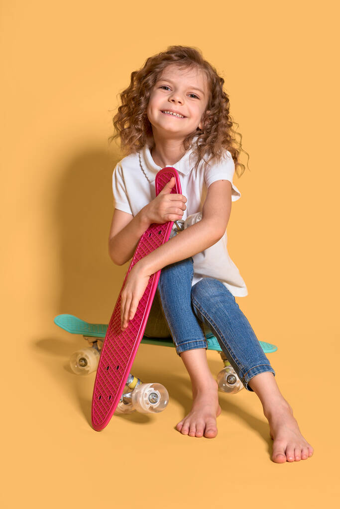 Aktivní a šťastný Kid baví s penny palubě, usmívající se tvář stojan skateboard. Penny palubě roztomilý skateboard pro dívky. Jdeme na to. Dívka jezdit penny palubě žluté pozadí. Letní dovolená - Fotografie, Obrázek