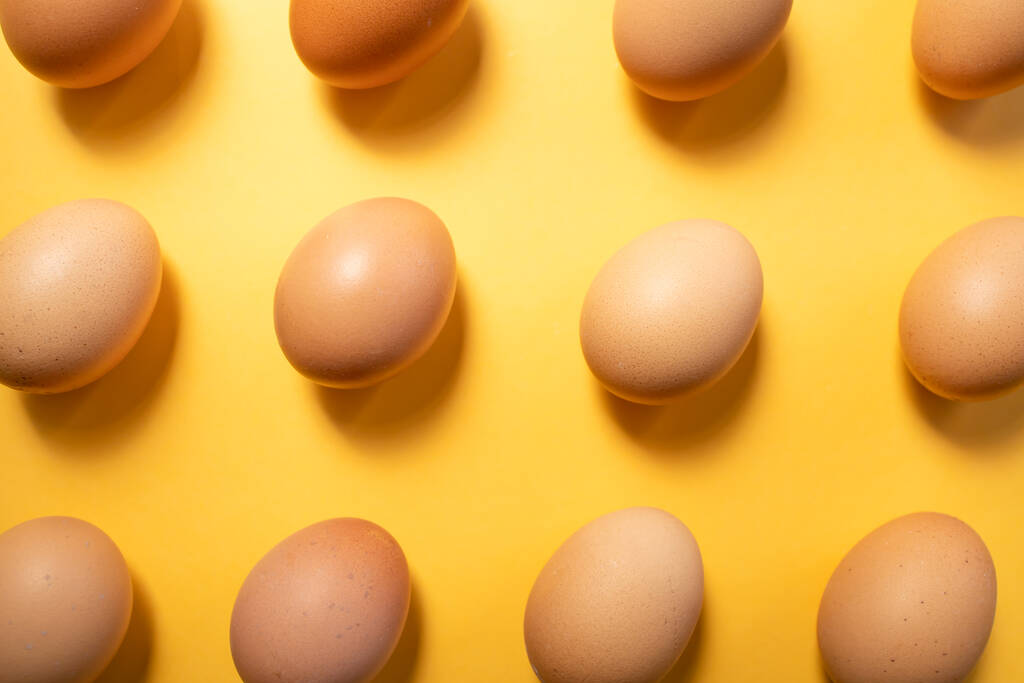 Φρέσκα αυγά ευθυγραμμισμένα στο κίτρινο φόντο άψογα. Η ιδέα του Πάσχα. Ιστορικό, πρότυπο - Φωτογραφία, εικόνα
