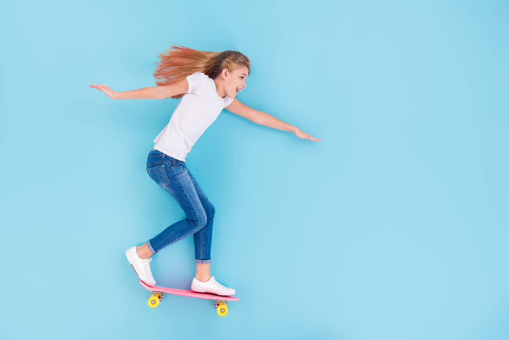 Сверху над высоким углом обзора фотография в полный рост возбужденной девочки, катающейся на скейтборде в пустом пространстве, наслаждающейся развлечениями, лежит на голубом цветном фоне
 - Фото, изображение