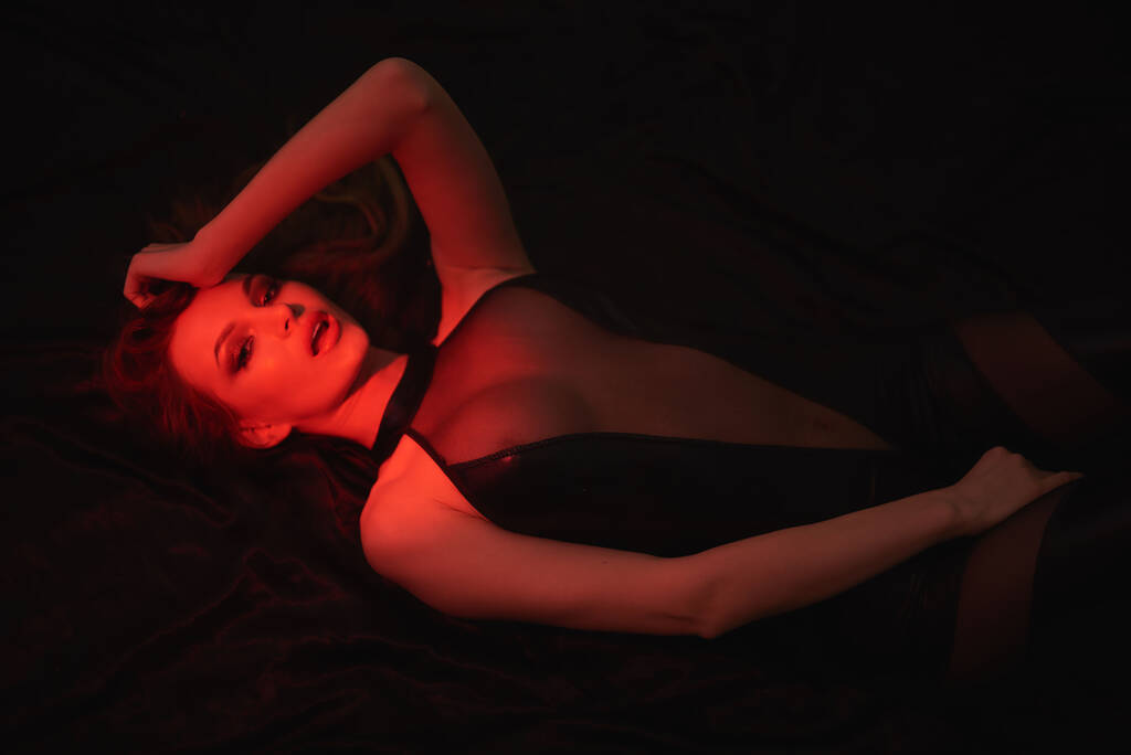 Sexy meid ligt op het bed in een sexy pak. Fotoshoot met een rood licht. - Foto, afbeelding