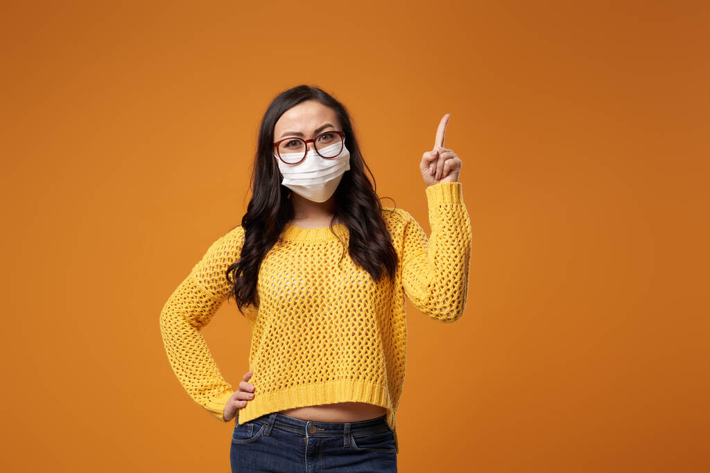 Chine kobieta w okularach i maska medyczna wskazując rękę w studio - Zdjęcie, obraz