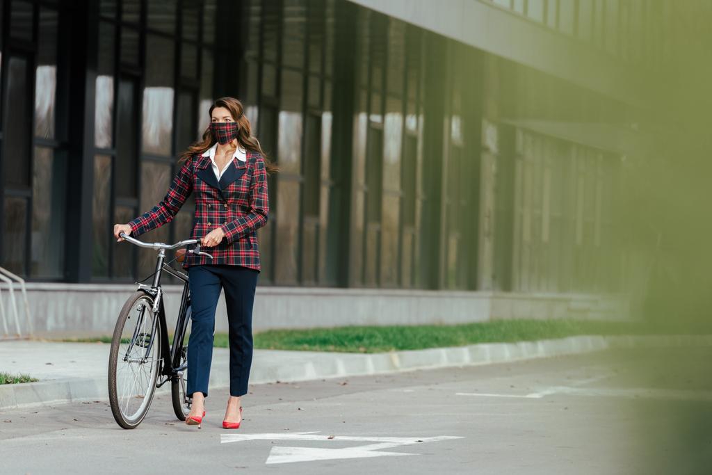 вибірковий фокус бізнес-леді в простій масці, що йде з велосипедом
  - Фото, зображення