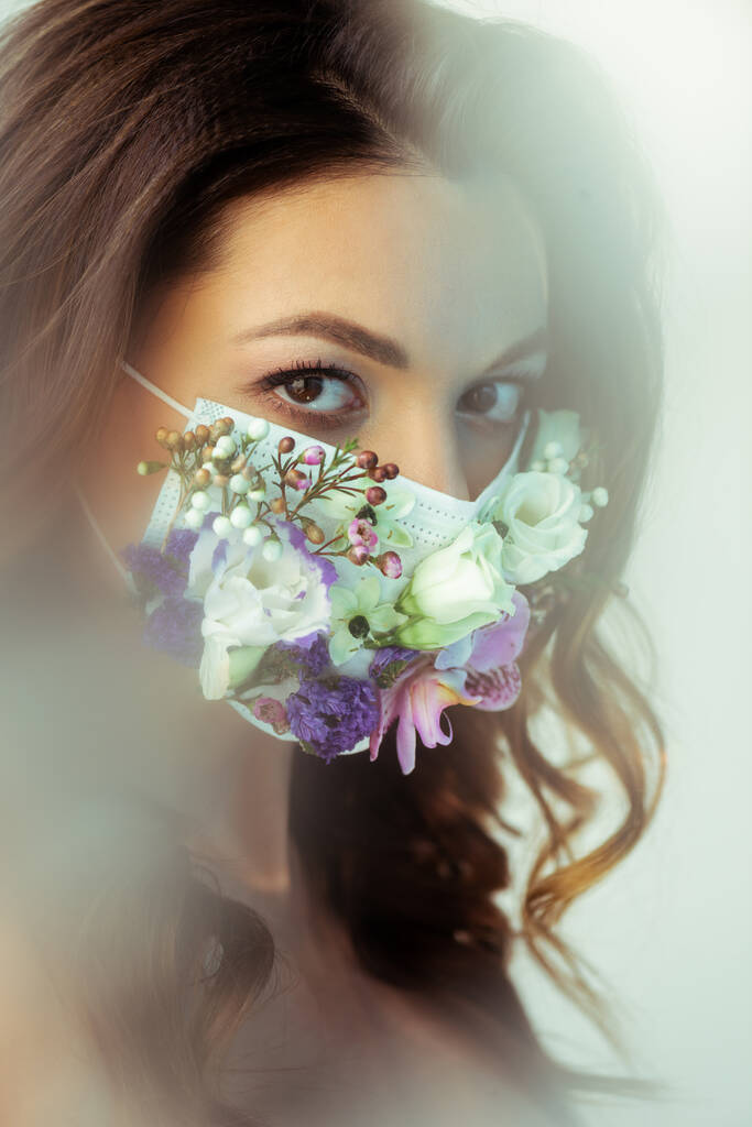 selective focus of woman in floral face mask looking at camera on white - Photo, Image