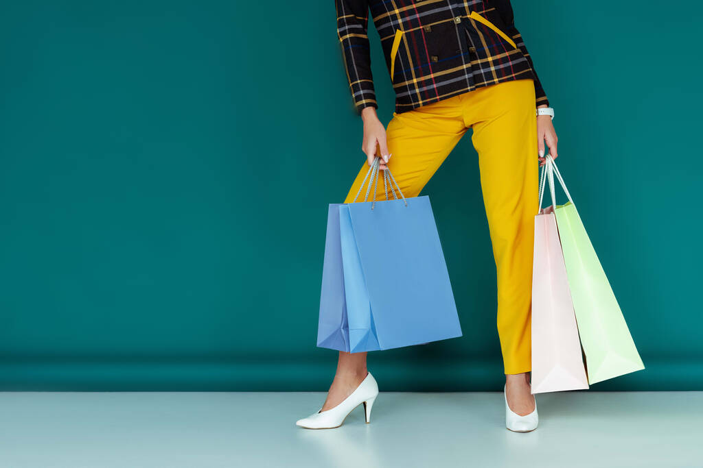 vista recortada de la mujer con estilo en chaqueta a cuadros de pie con bolsas de compras en azul
 - Foto, imagen