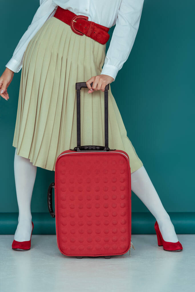 обрезанный вид на стильную девушку, стоящую с чемоданом на синем
  - Фото, изображение