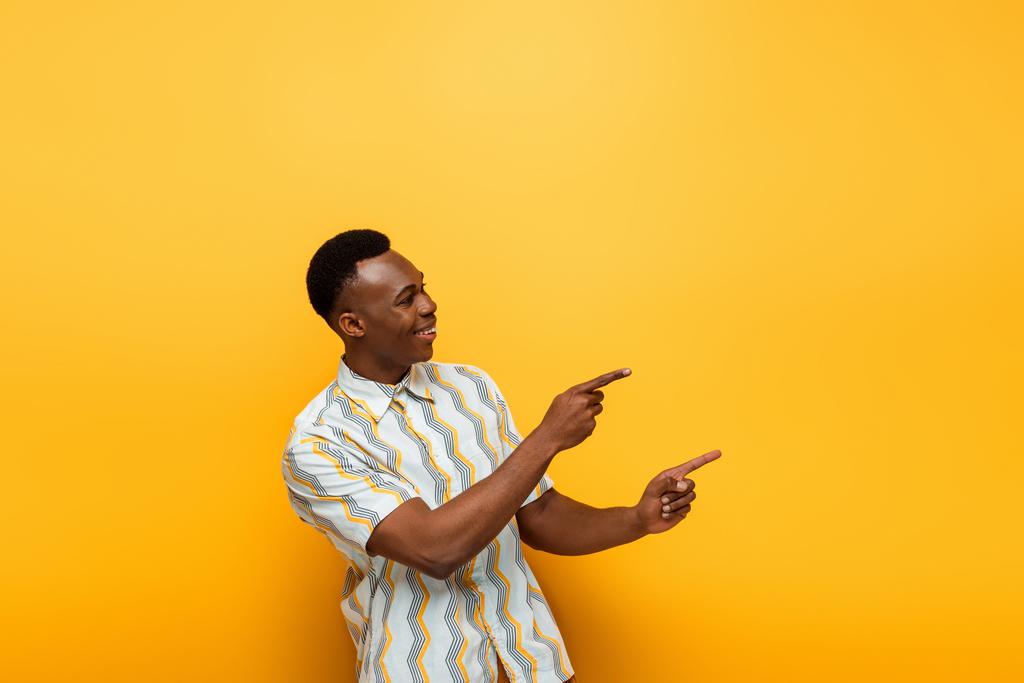 gelukkig Afrikaans amerikaanse man wijzend met vingers op gele achtergrond - Foto, afbeelding