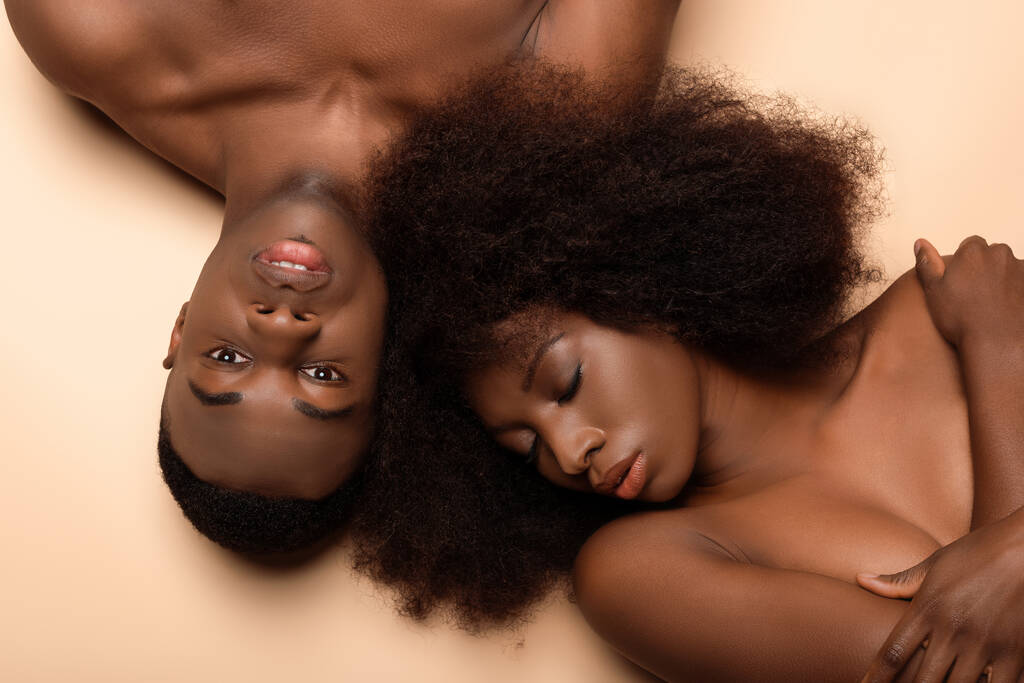 セクシーな裸のアフリカ系アメリカ人のカップルがベージュに目を閉じたまま横たわっています - 写真・画像