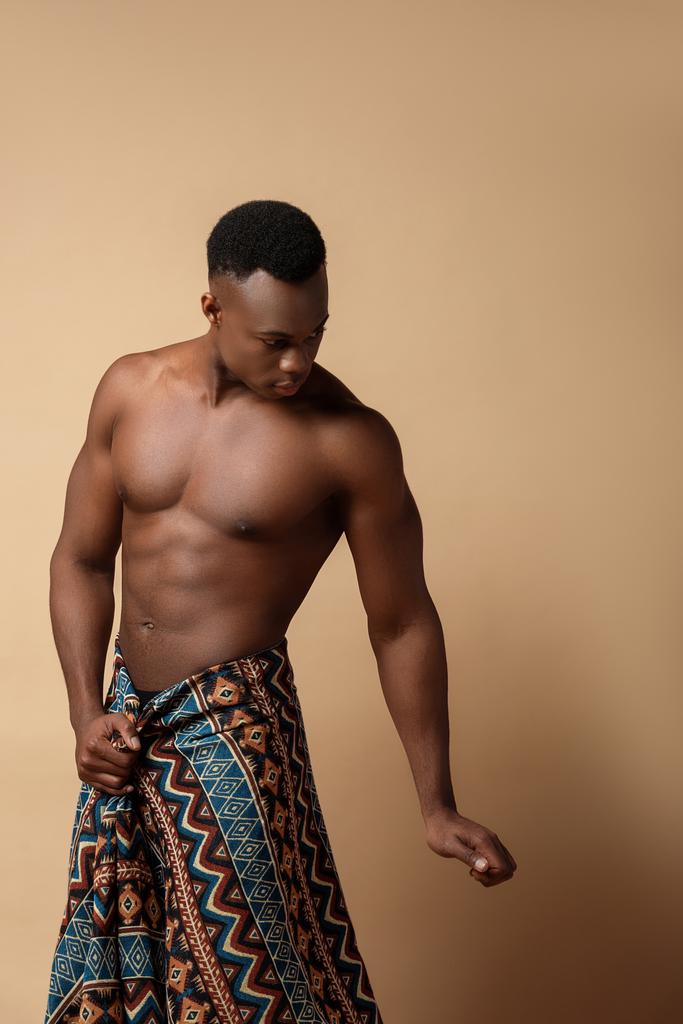 sexy nudo tribale afro uomo coperto in coperta posa su beige
 - Foto, immagini
