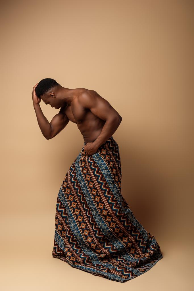 sexy nackten Stammes Afro-Mann in Decke bedeckt posiert auf beige - Foto, Bild