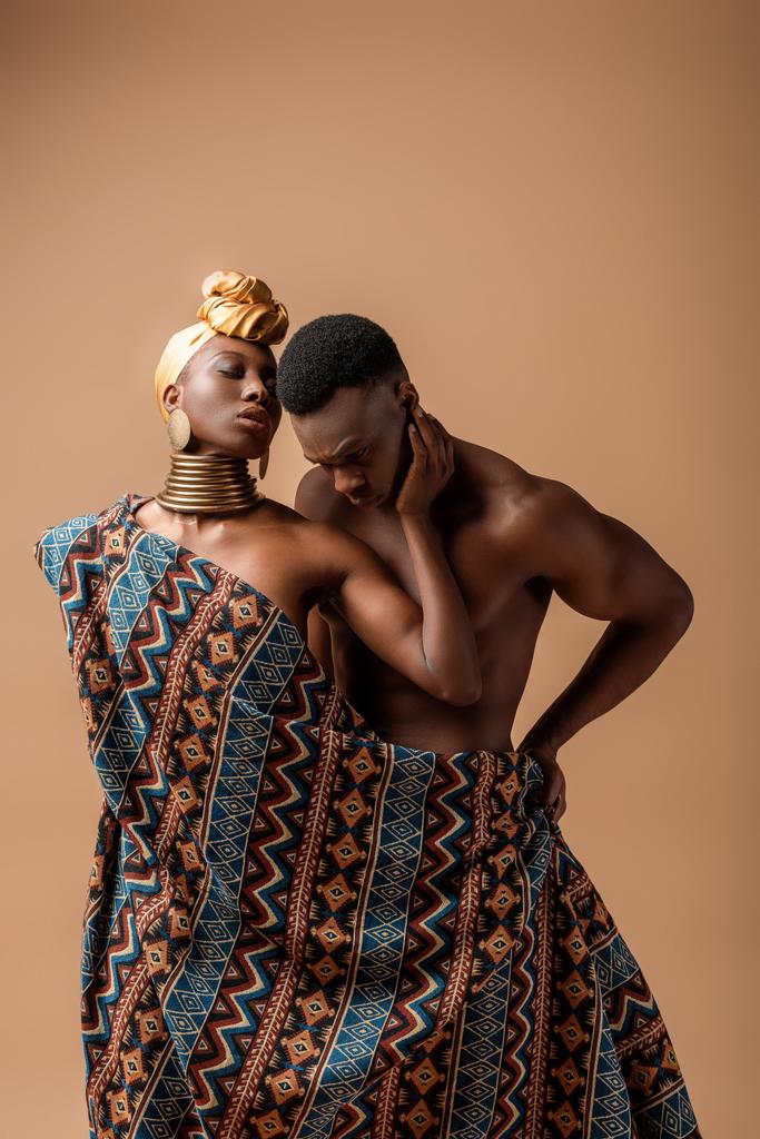 sexy nagi plemienny afro kobieta pokryte w koc pozowanie obok mężczyzna na beżowy - Zdjęcie, obraz