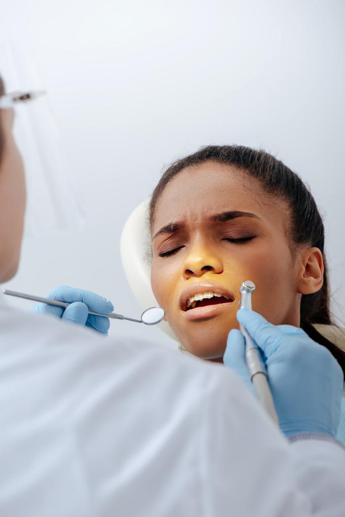 селективний фокус ортодонта в латексних рукавичках, що тримає зубні інструменти поблизу засмученої афроамериканської жінки в брекетах
  - Фото, зображення