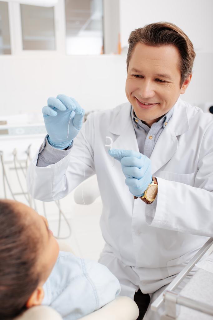 幸せな歯科医がアフリカ系アメリカ人女性の近くに歯科フロスを持ち  - 写真・画像