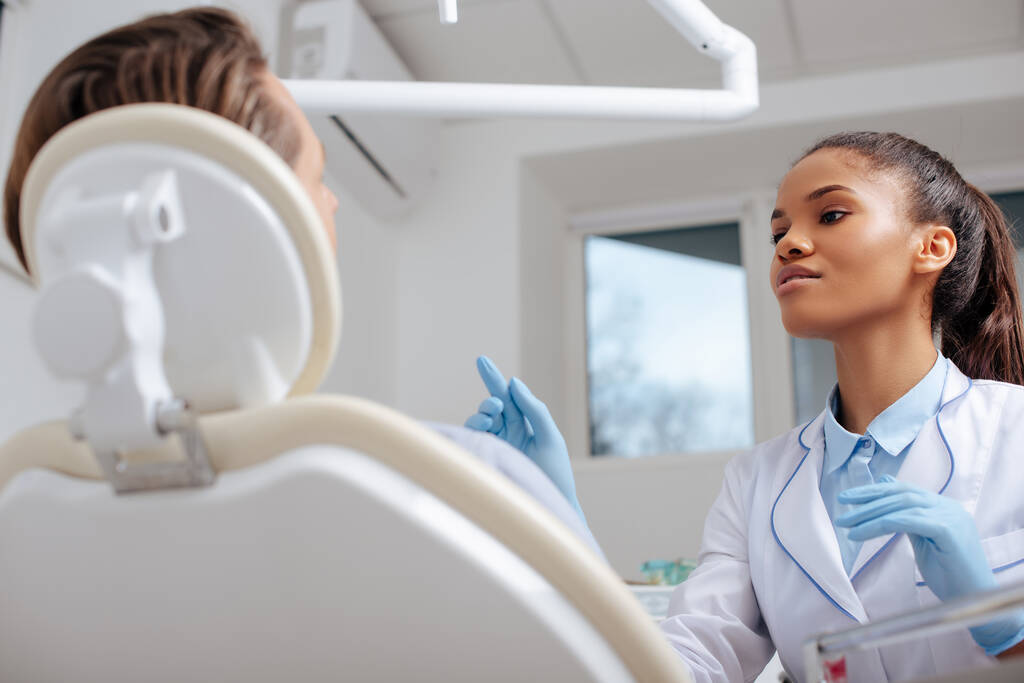 messa a fuoco selettiva di attraente dentista afroamericano che punta con il dito vicino al paziente
  - Foto, immagini