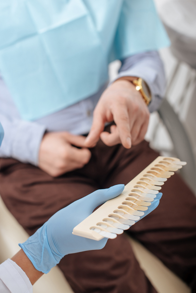oříznutý pohled muže ukazujícího prstem na paletu zubů u zubaře v latexových rukavicích - Fotografie, Obrázek