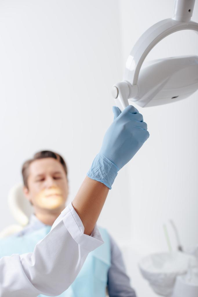 患者の近くの医療用ランプに触れるラテックス手袋のアフリカ系アメリカ人歯科医の選択的焦点  - 写真・画像
