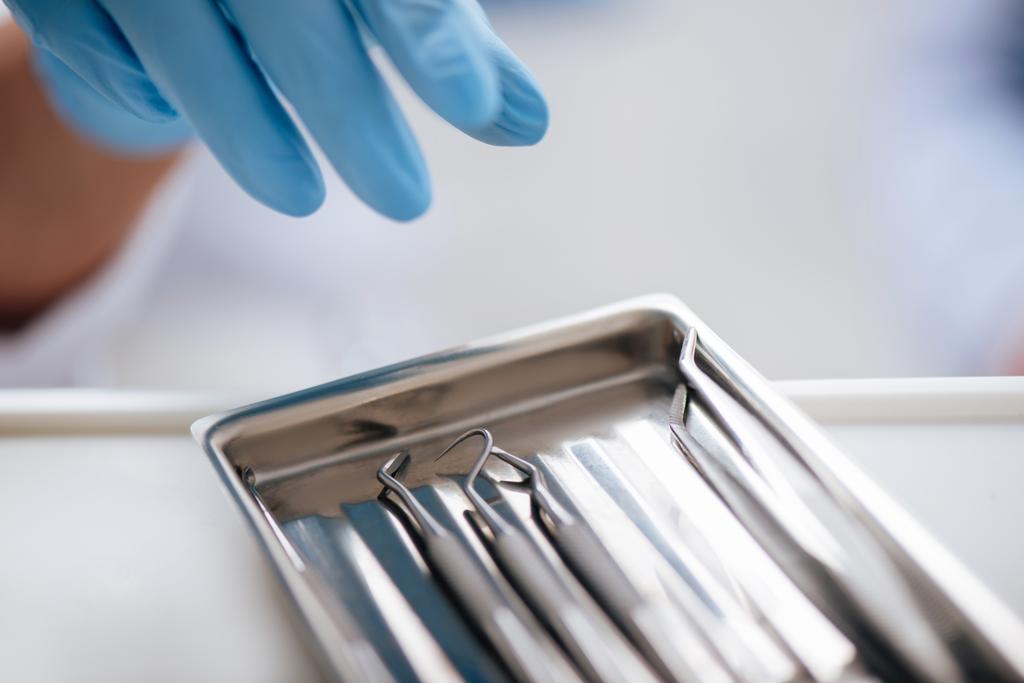 przycięty widok rentista w rękawicy lateksowej sięgający po instrumenty dentystyczne ze stali nierdzewnej  - Zdjęcie, obraz