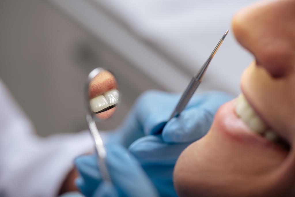 bijgesneden beeld van tandarts in latex handschoenen met tandheelkundige instrumenten in de buurt van glimlachende man  - Foto, afbeelding