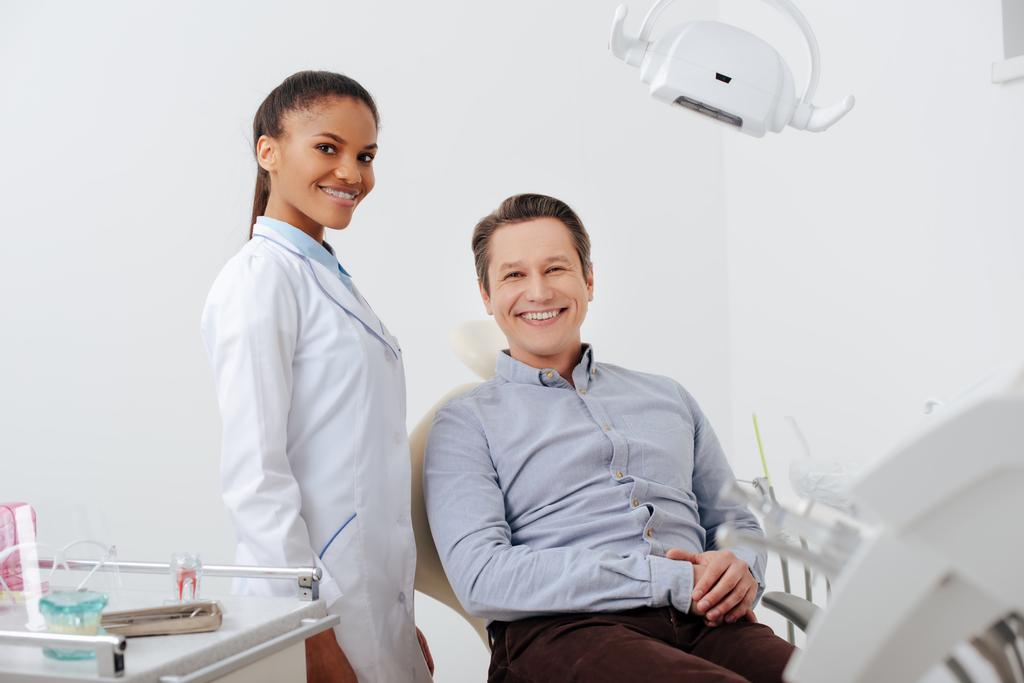Selektiver Fokus glücklicher Patienten mit fröhlichem afrikanisch-amerikanischem Zahnarzt in Zahnspange - Foto, Bild