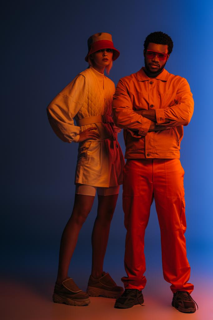 moda casal interracial posando em olhar futurista no azul em luz laranja
 - Foto, Imagem