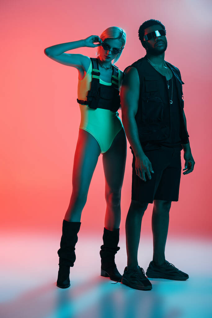 interracial couple posing in futuristic look and sunglasses on pink - Photo, Image