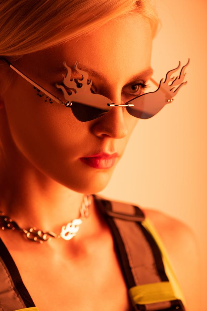 стильная футуристическая модель, позирующая в огнеобразных солнцезащитных очках на оранжевом
 - Фото, изображение