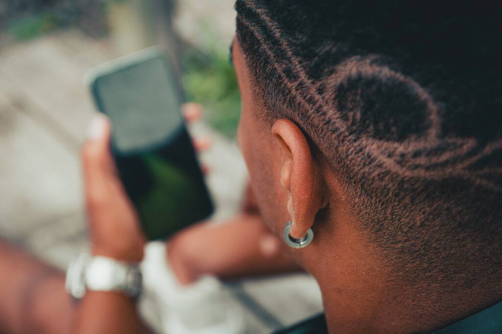 Schöne Aufnahme eines jungen Mannes mit cooler Frisur, der in einem Park auf sein Handy starrt - Foto, Bild