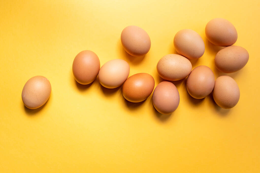 Group of fresh eggs on the table isolated on yellow background. Easter concept. - Photo, Image