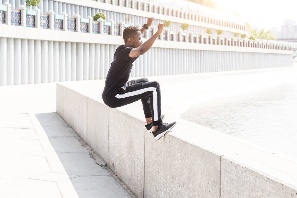 Sportowy młody Afroamerykanin biegający po promenadzie. Czarny biegacz biegnie na zewnątrz. Koncepcja zdrowego stylu życia. - Zdjęcie, obraz