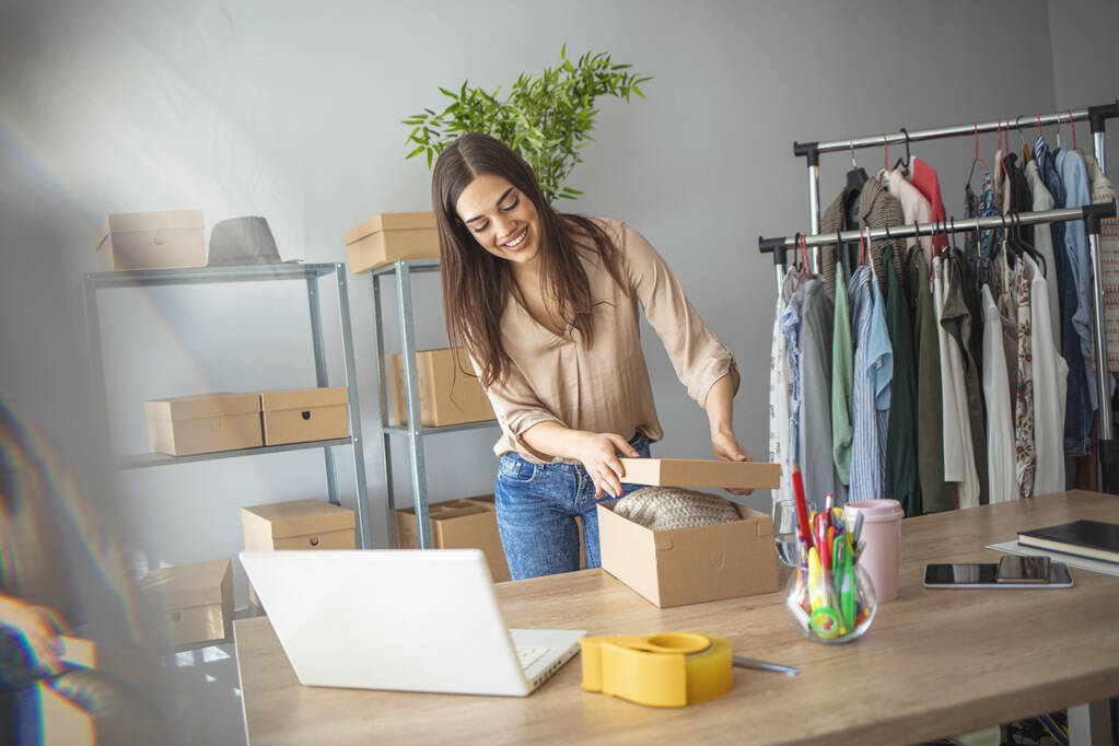 Young woman selling products online and packaging goods for shipping. Women, owener of small business packing product in boxes, preparing it for delivery - Photo, Image