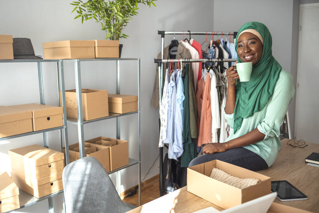 Muslimische Modedesignerin in ihrem Geschäft. Frauen, Inhaber von Kleinunternehmen, verpacken Produkte in Kisten und bereiten sie für die Auslieferung vor. Frau packt Artikel ein, die sie online verkauft - Foto, Bild