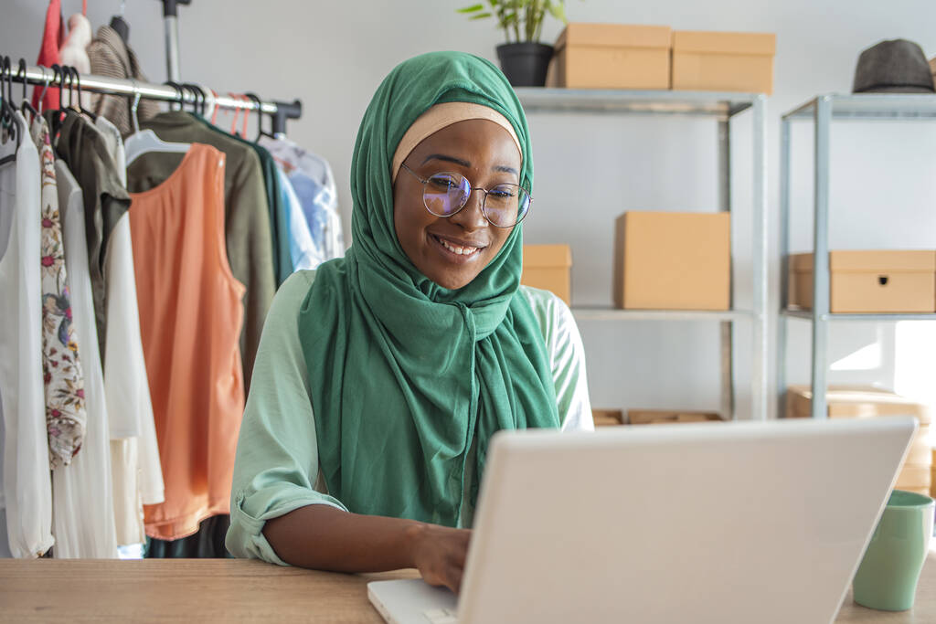 Muslimische Frau führt ein kleines Geschäft in ihrem eigenen Haus. Ist das Design und die Schneiderei von Kleidung. Glückliche schöne muslimische Geschäftsfrau, die mit Geschäftsbericht und Taschenrechner im Homeoffice über Finanzen arbeitet - Foto, Bild